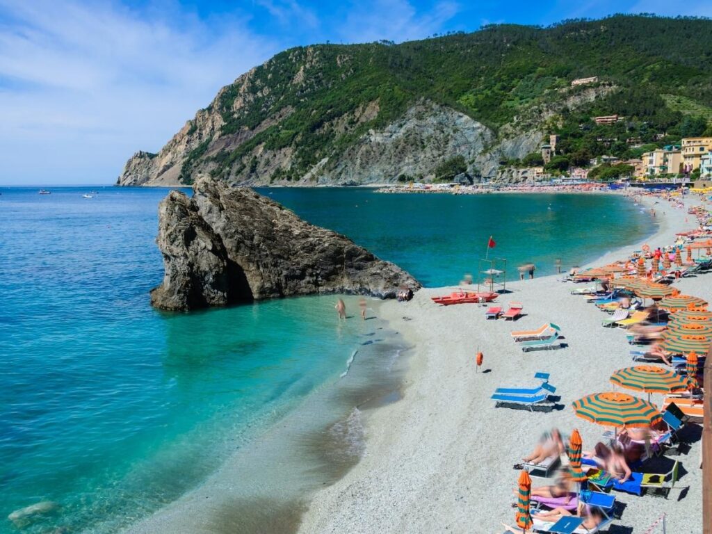 Monterosso beachfront with families, umbrellas, and swimmers in the sea.