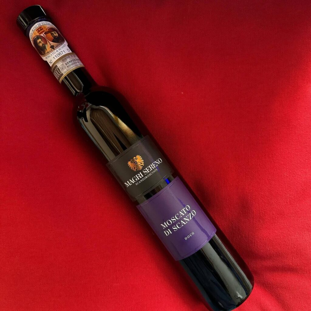 A glass of Moscato di Scanzo sweet red wine on a wooden table with vineyard views.