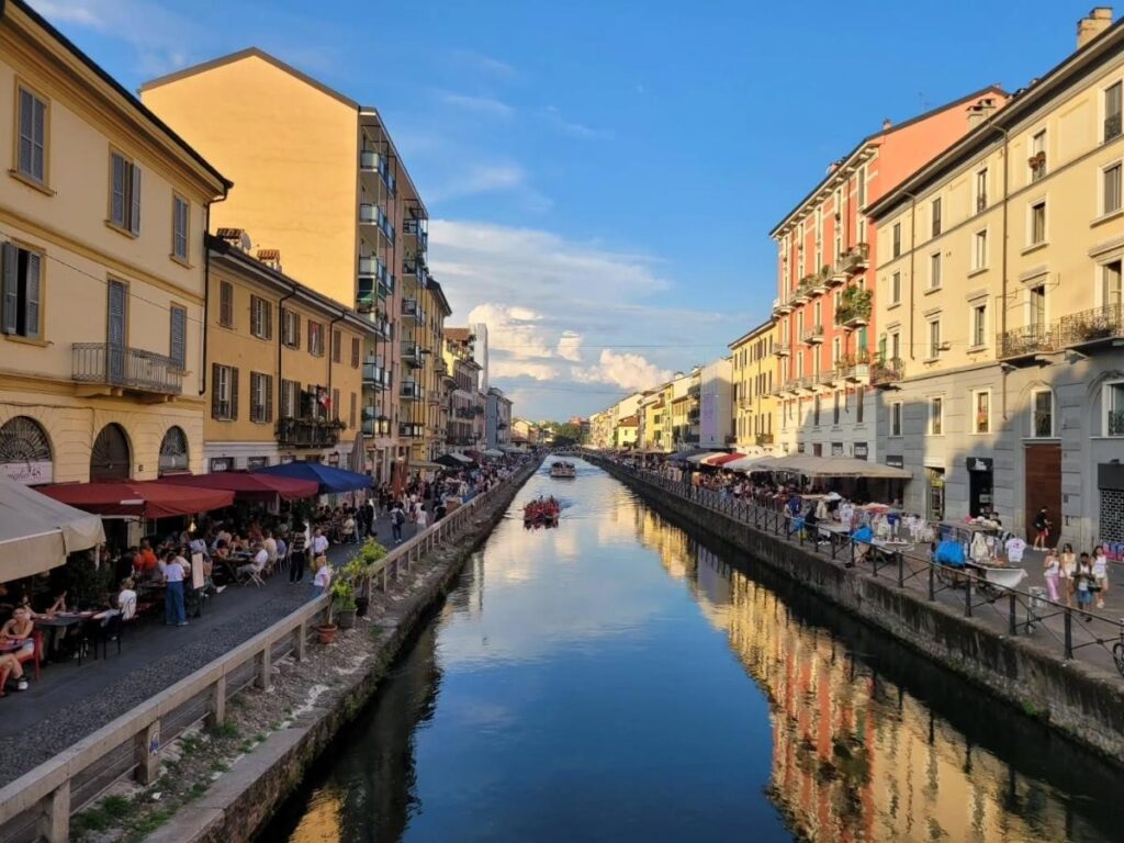 People enjoying aperitivo on terrace tables along Navigli canal at sunset.