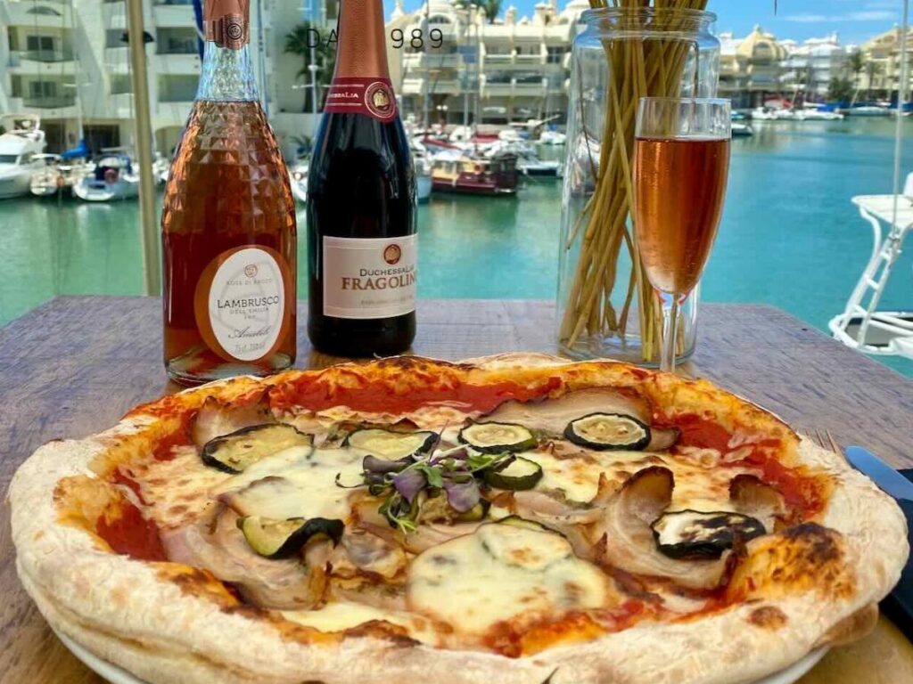 Outdoor trattoria table in Pisa with pasta, white wine, and view of the Arno River.