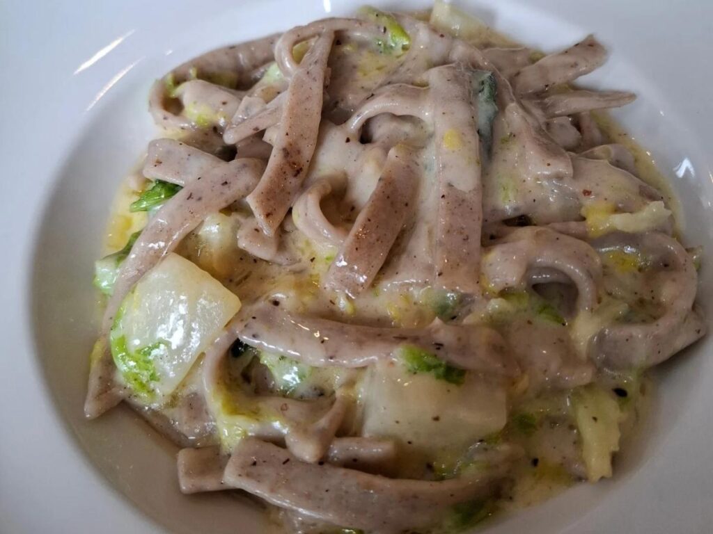Bowl of pizzoccheri served in a rustic trattoria with local cheese and herbs.