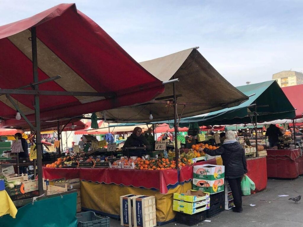 Stalls with fresh vegetables and vendors at Porta Palazzo market in Turin