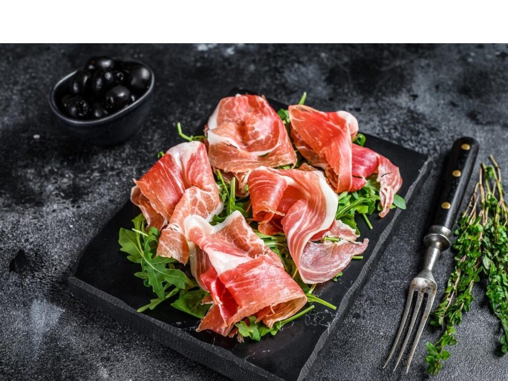 Thin slices of Prosciutto di Parma served on a wooden board with Lambrusco wine."