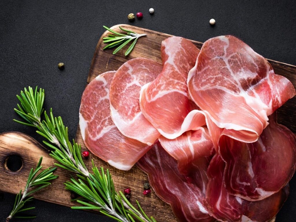 Paper-thin slices of Prosciutto di San Daniele on a wooden cutting board