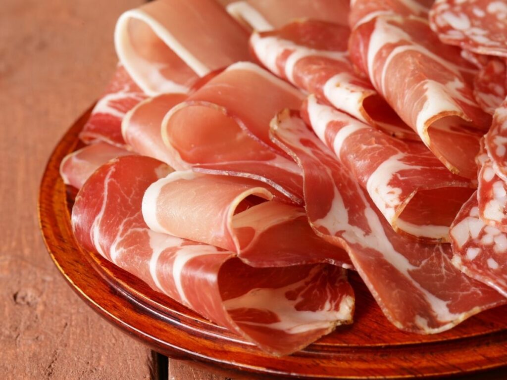 Paper-thin slices of Prosciutto di San Daniele on a wooden board.