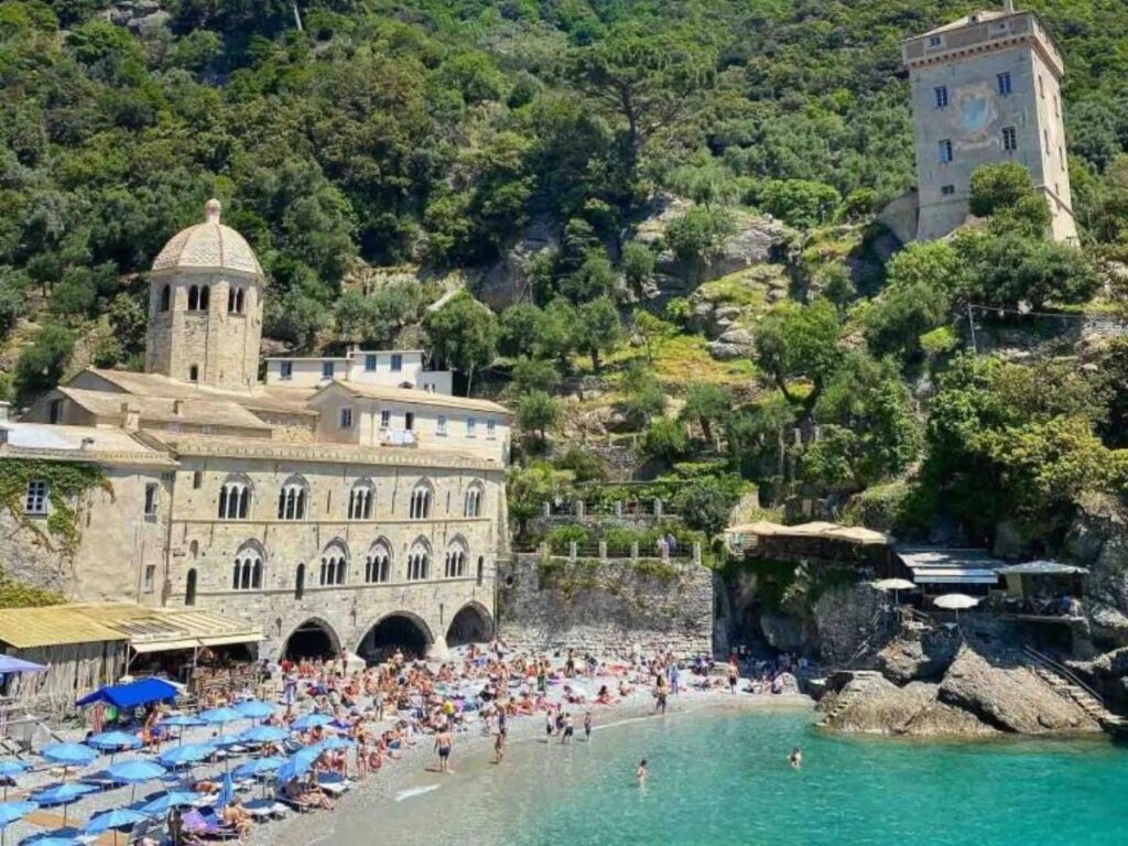 San Fruttuoso Abbey framed by green hills and pebble beach, photographed from a boat.
