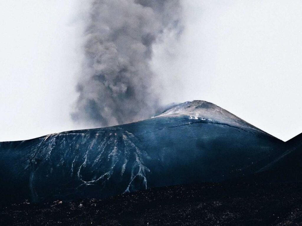 Hiker walking across a black lava field on the lower slopes of Mount Etna.