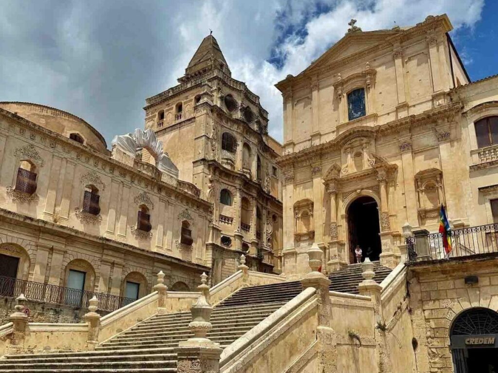 Golden-hour façade of a baroque church in Noto with warm-lit stone and blue sky.