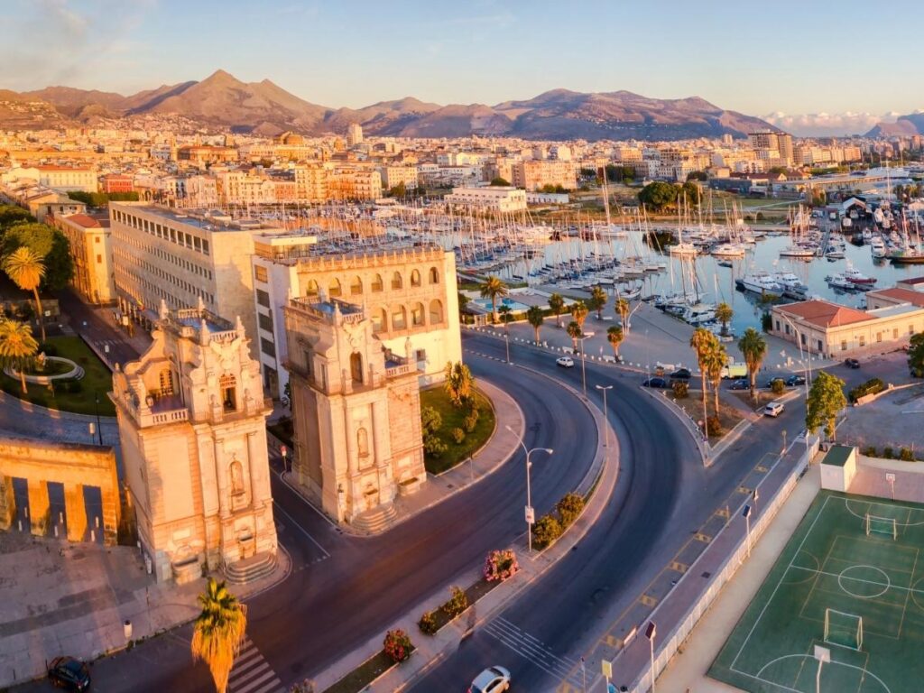 Charming boutique hotel courtyard in Palermo with stone walls, potted plants, and cozy seating.