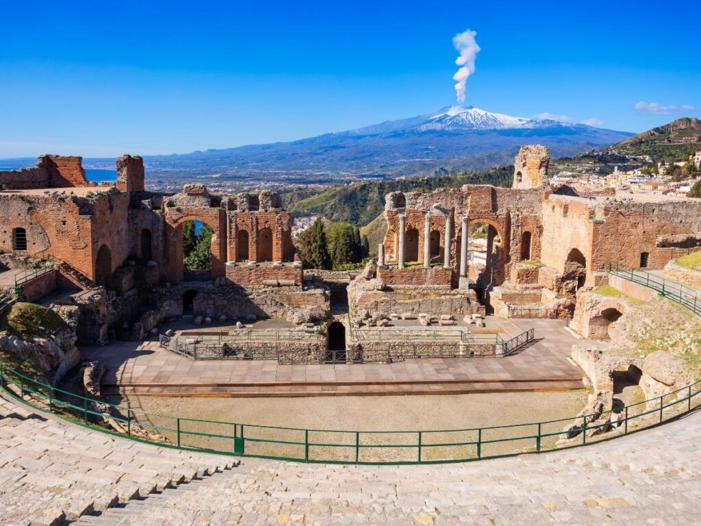 Luxury hotel terrace in Taormina overlooking the Ionian Sea with Mount Etna in the distance.