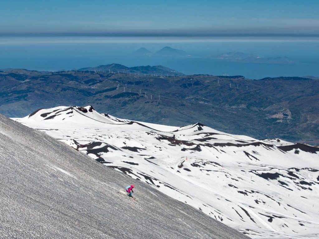 Skiers at Piano Provenzana with snowy volcanic slopes and the Mediterranean Sea in view