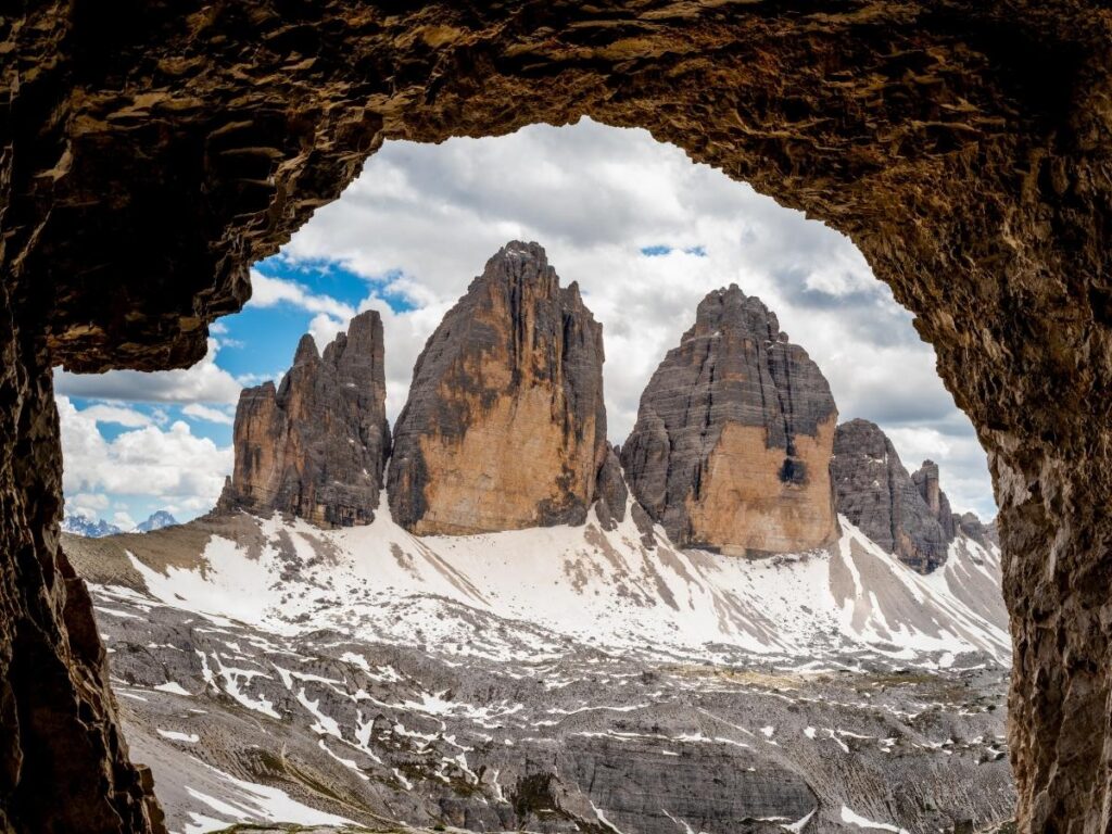 Tre Cime di Lavaredo peaks at golden hour, seen from the hiking loop with foreground rocks and trail.