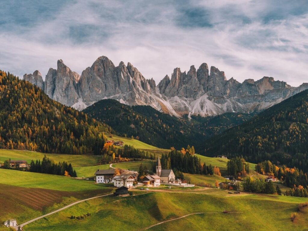 The church of St. Magdalena in Val di Funes with green meadows and dramatic Dolomite peaks behind it.
