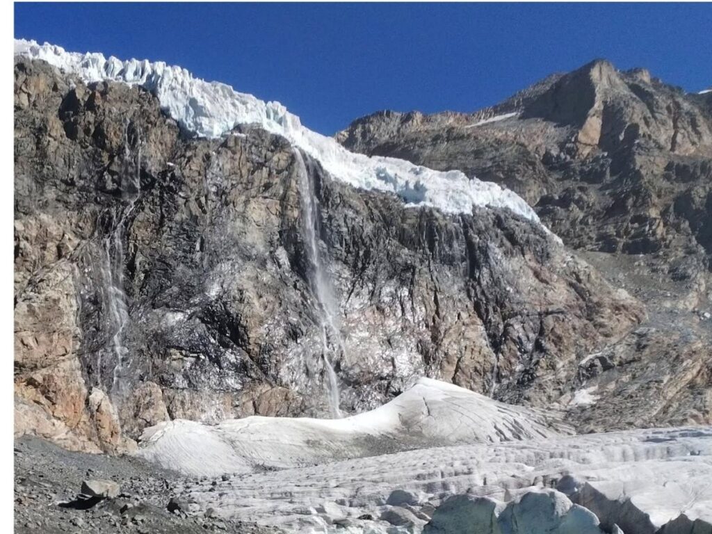 Alpine trail in the Valtellina Valley with stone houses and peaks in the distance.
