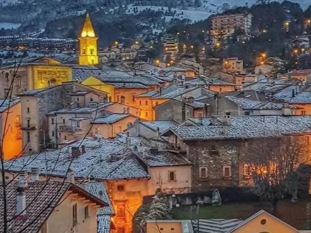 Locals chatting at outdoor tables in a small Abruzzo piazza as streetlights warm the scene.