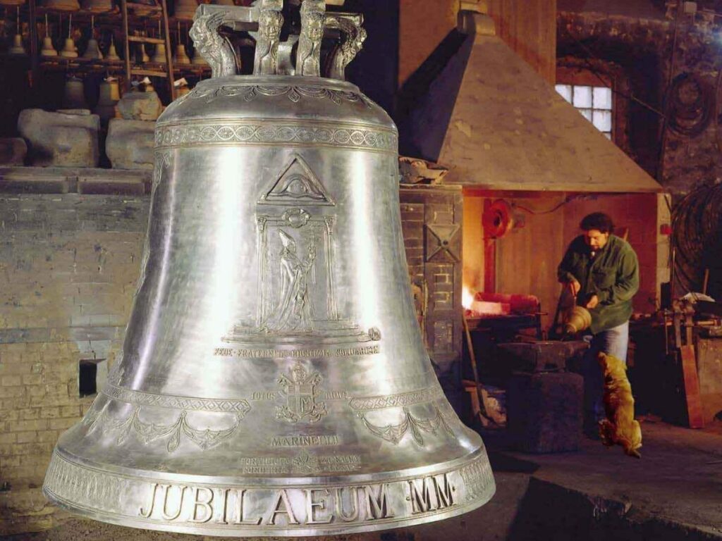 Inside a traditional bell foundry in Agnone showing a large bell and a craftsman at work.