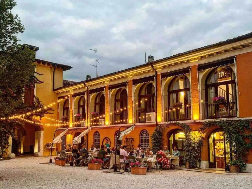 Long table set outdoors at an agriturismo with people sharing homemade dishes and wine.