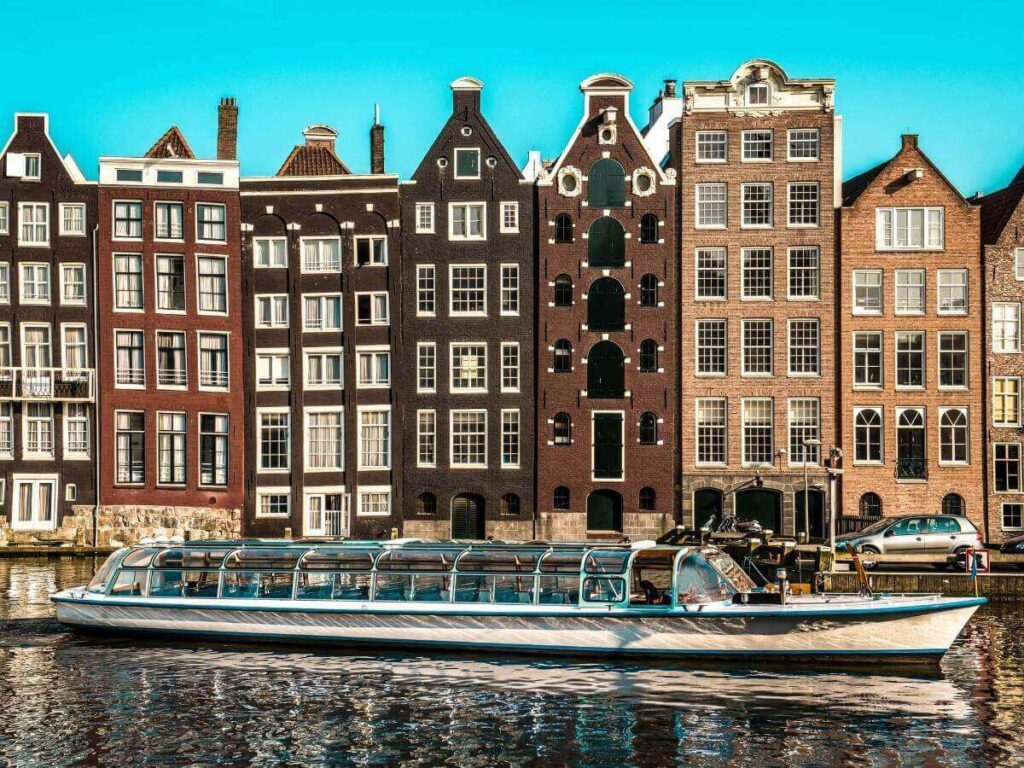Small open canal boat gliding under a bridge lined with bicycles and flowers in Amsterdam