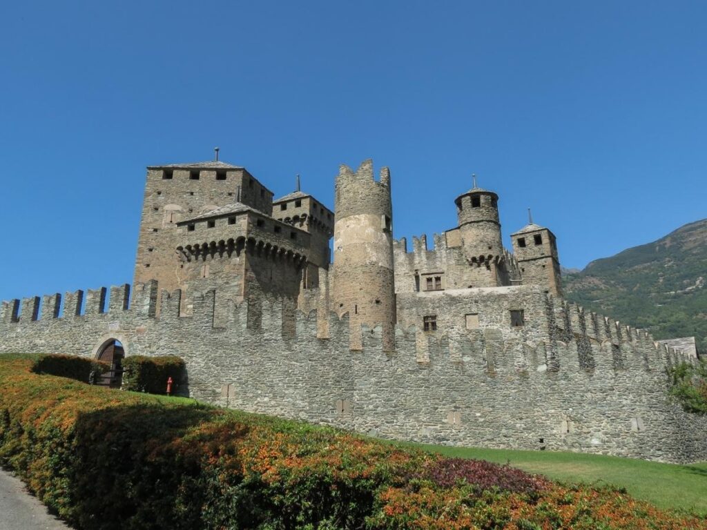 Stone courtyard of Fénis Castle with medieval frescoes on the walls and mountain backdrop.