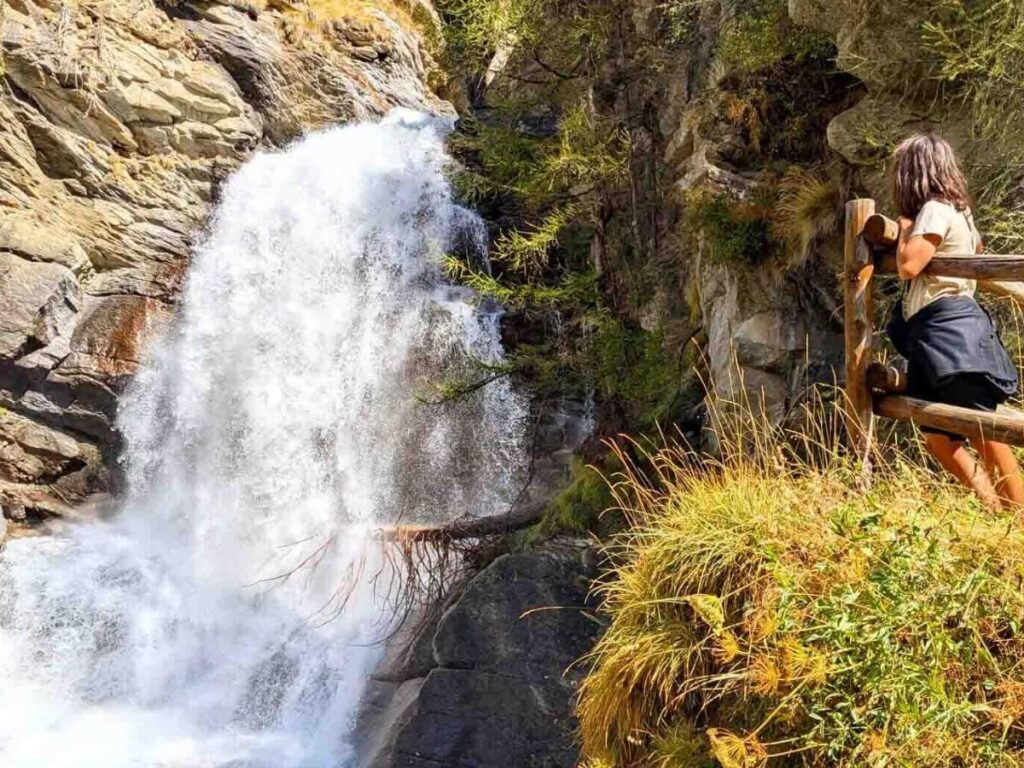 Lillaz Waterfalls framed by pine trees with water cascading over rocks into a clear alpine pool.