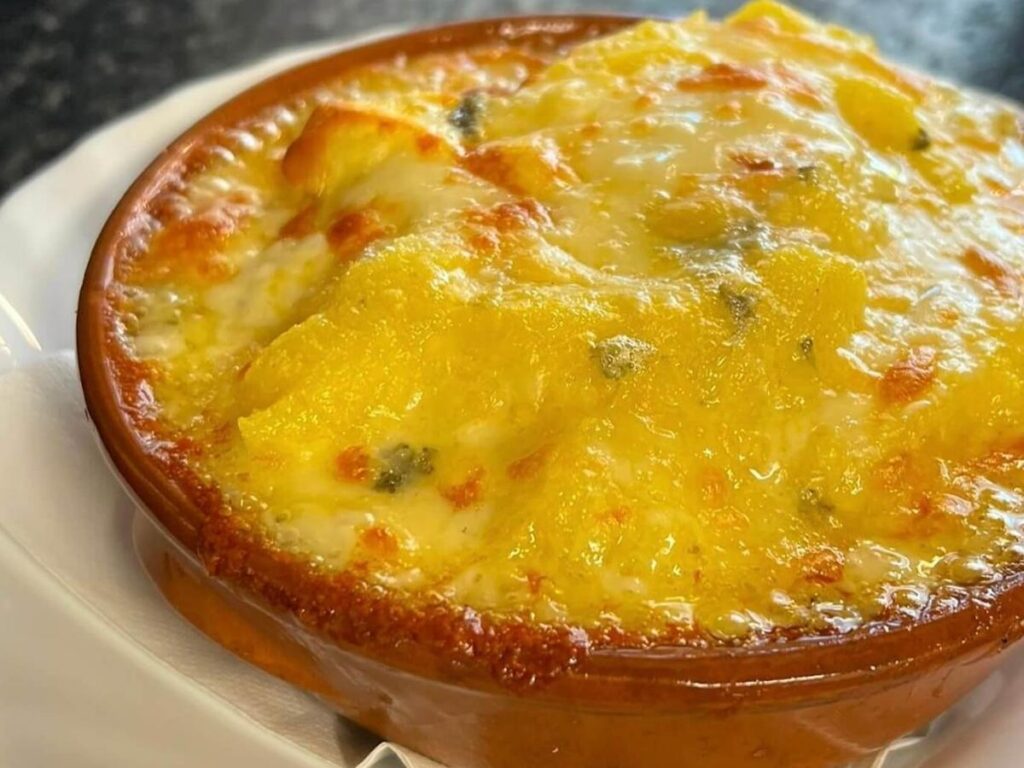 Traditional polenta concia baked with melted Fontina cheese served in a rustic clay dish, golden and bubbling hot.