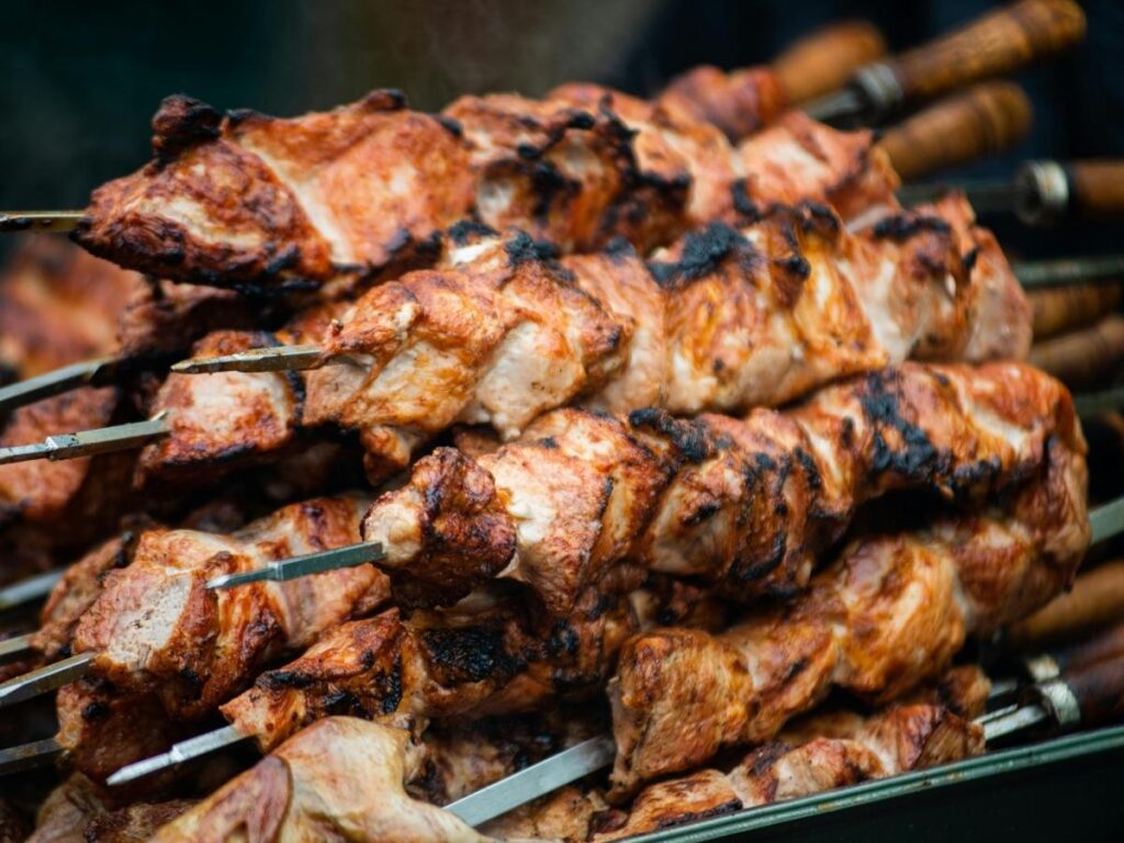 Dozen arrosticini lamb skewers in a paper cone, smoke rising from the grill — local street-food scene
