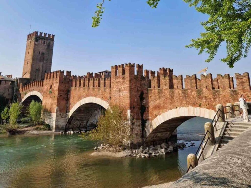 Castelvecchio fortress and bridge reflecting in the Adige River at golden hour.