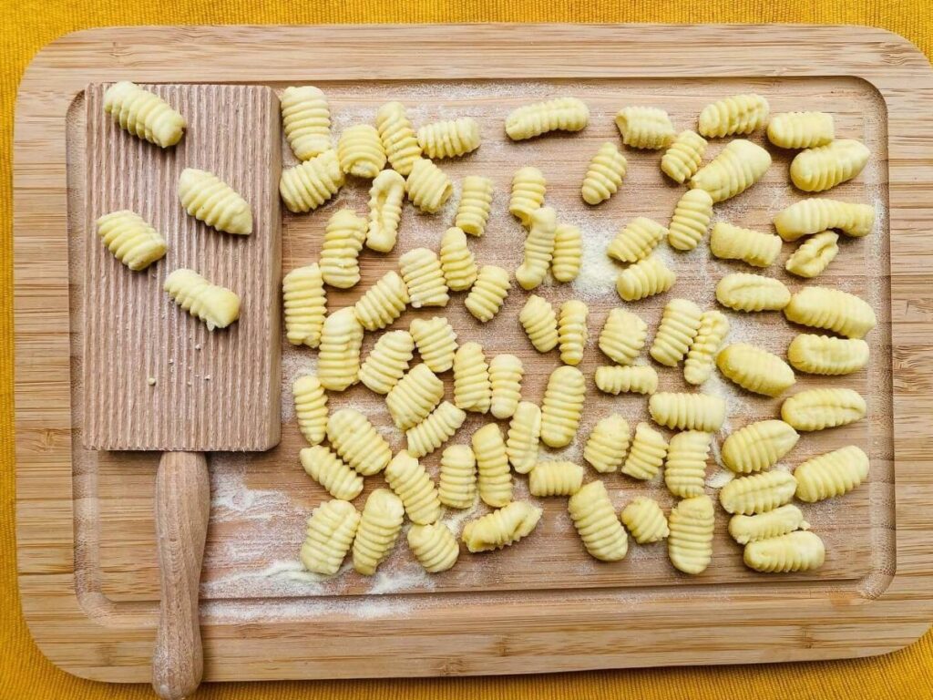 Close-up of handmade cavatelli pasta tossed in ragù on a ceramic plate.