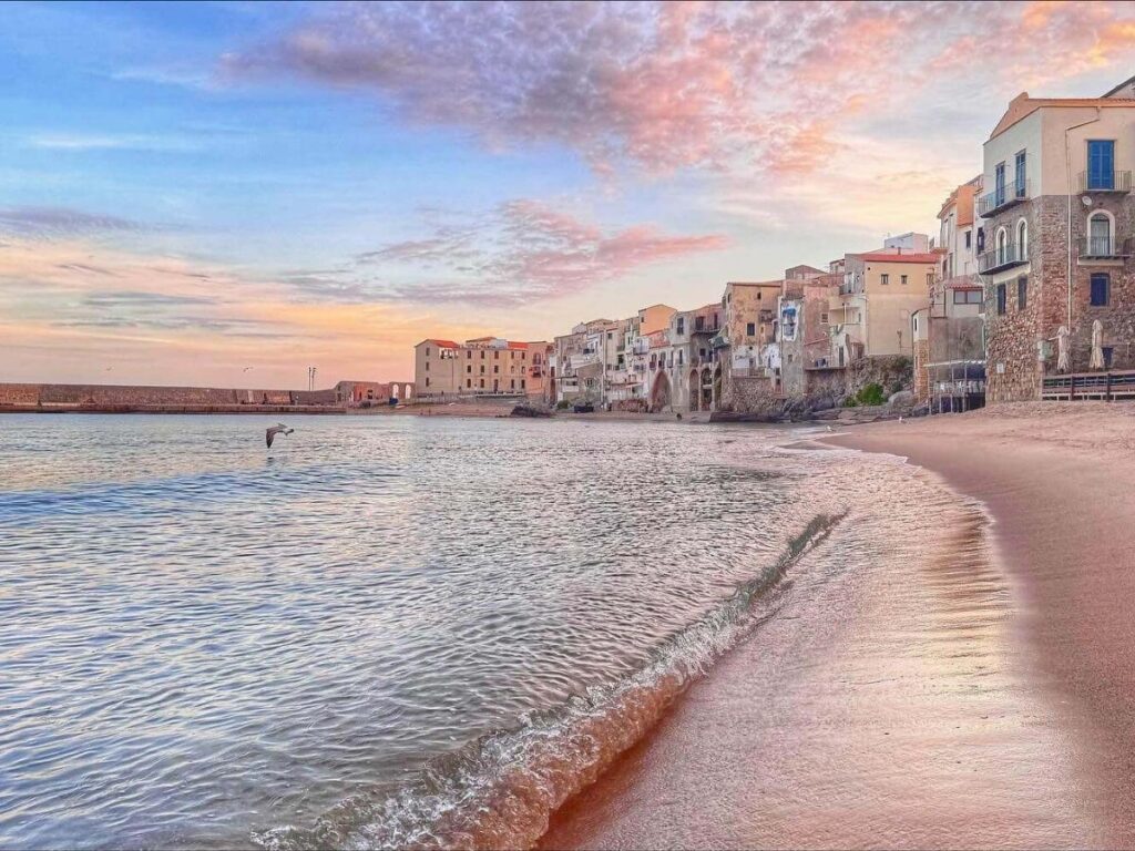 Colorful houses and fishing boats along Cefalù beach with La Rocca cliff in the background