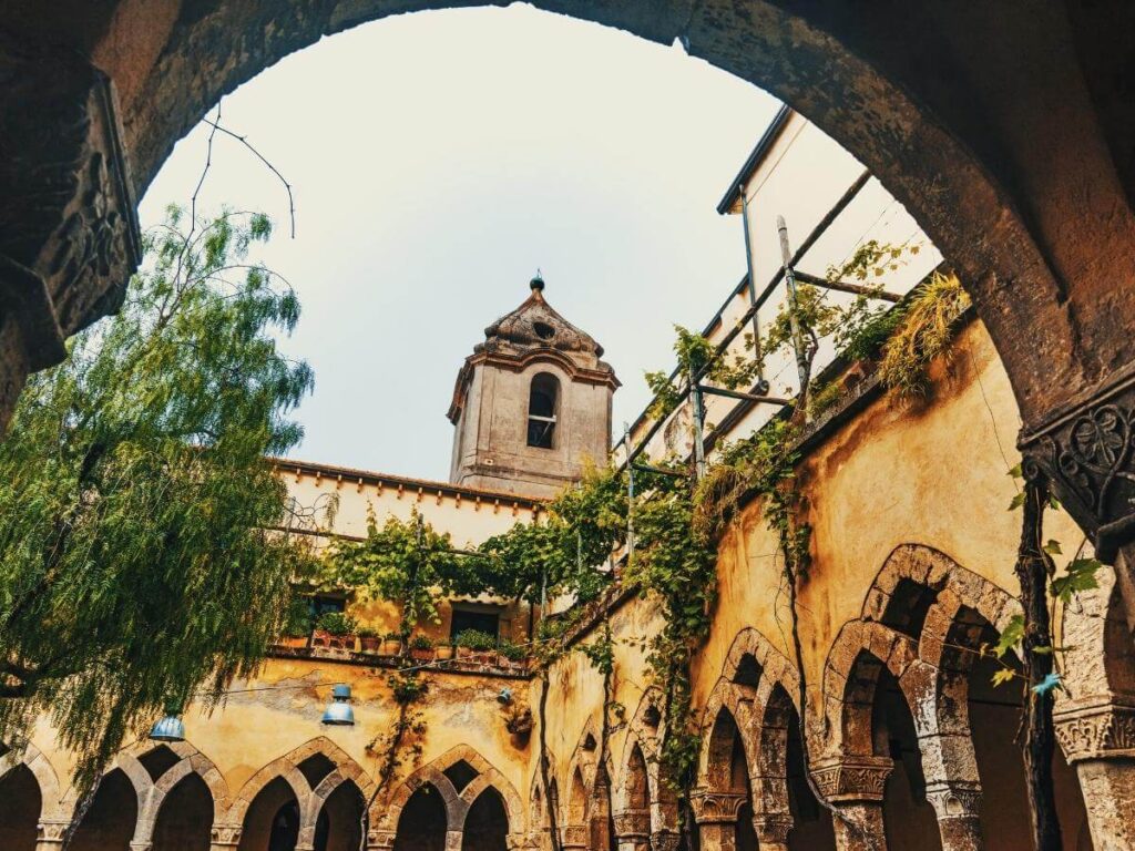 Stone arches covered in green vines at the peaceful Cloisters of San Francesco in Sorrento.