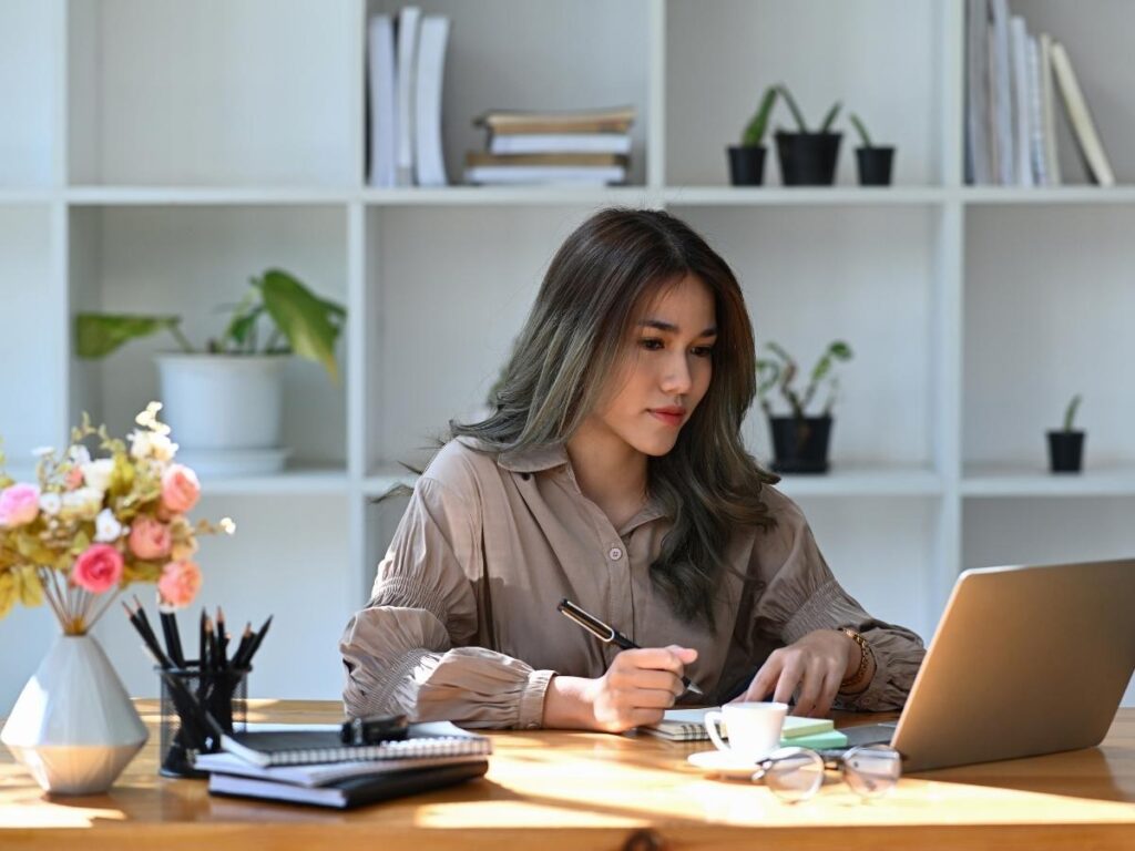 A woman sitting at a cozy desk with a laptop and travel brochures, booking a vacation early