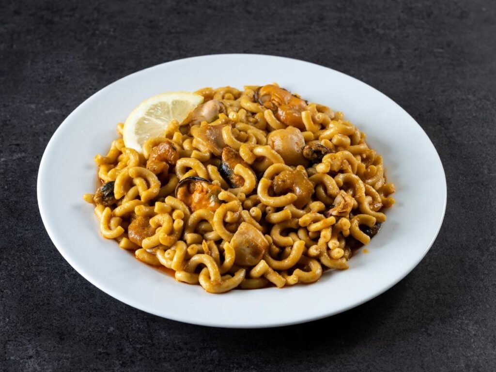 Catalan seafood fideuà in a paella pan with lemon wedges