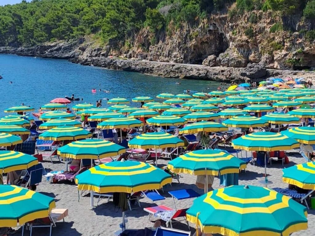 Families and locals relaxing on Fiumicello beach with umbrellas and calm blue water.