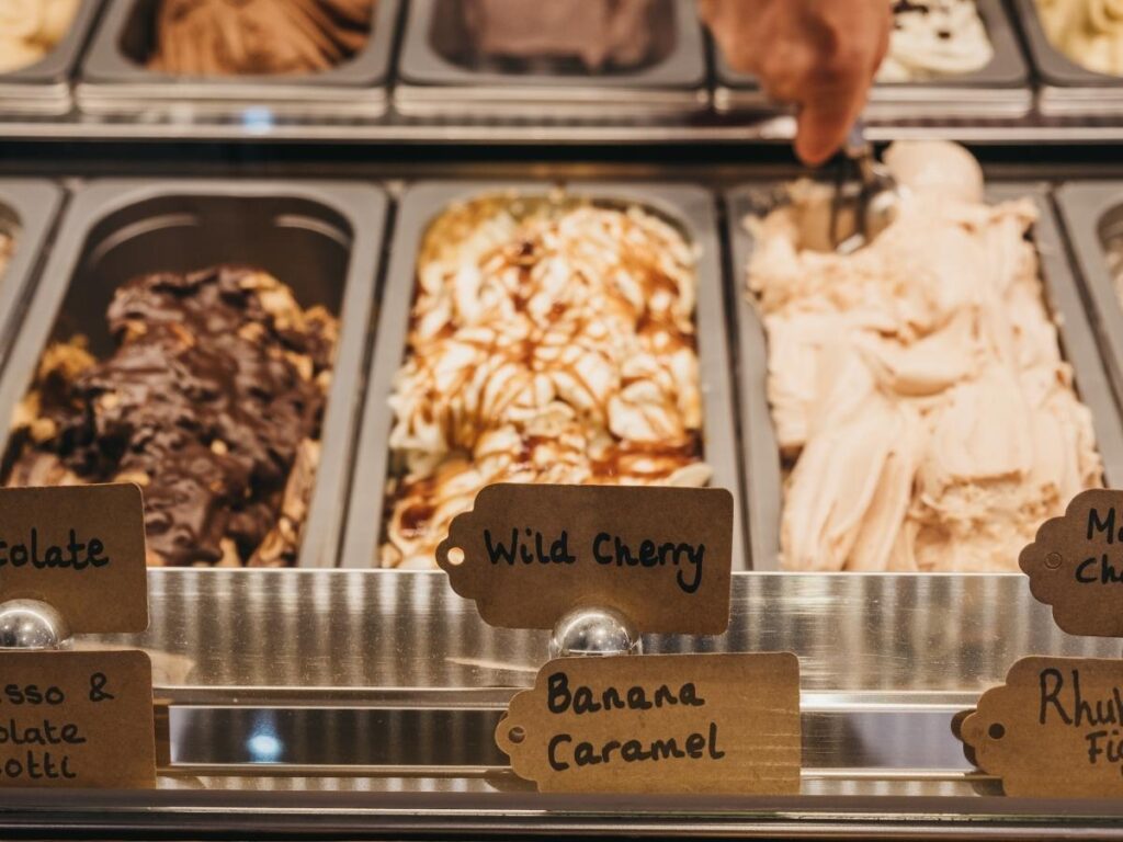 Artisan gelato in a waffle cone held up in Piazza Vittorio Emanuele, Lazise, with pastel buildings in the background
