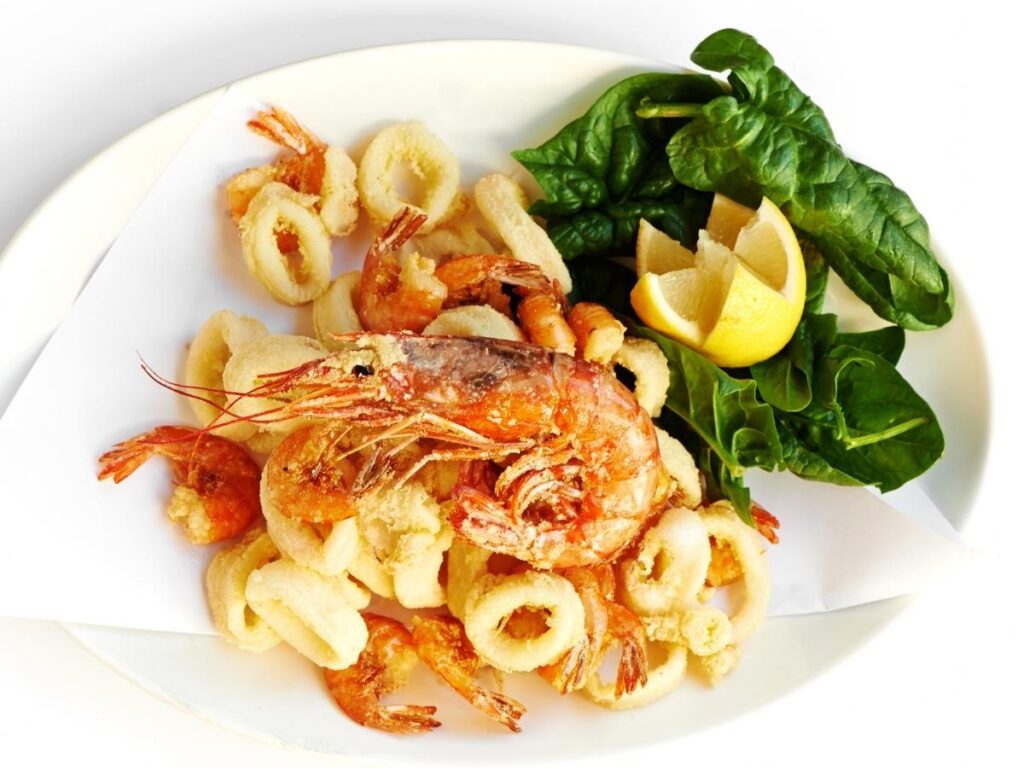 Plate of golden fritto misto with lemon wedges and a glass of Prosecco.