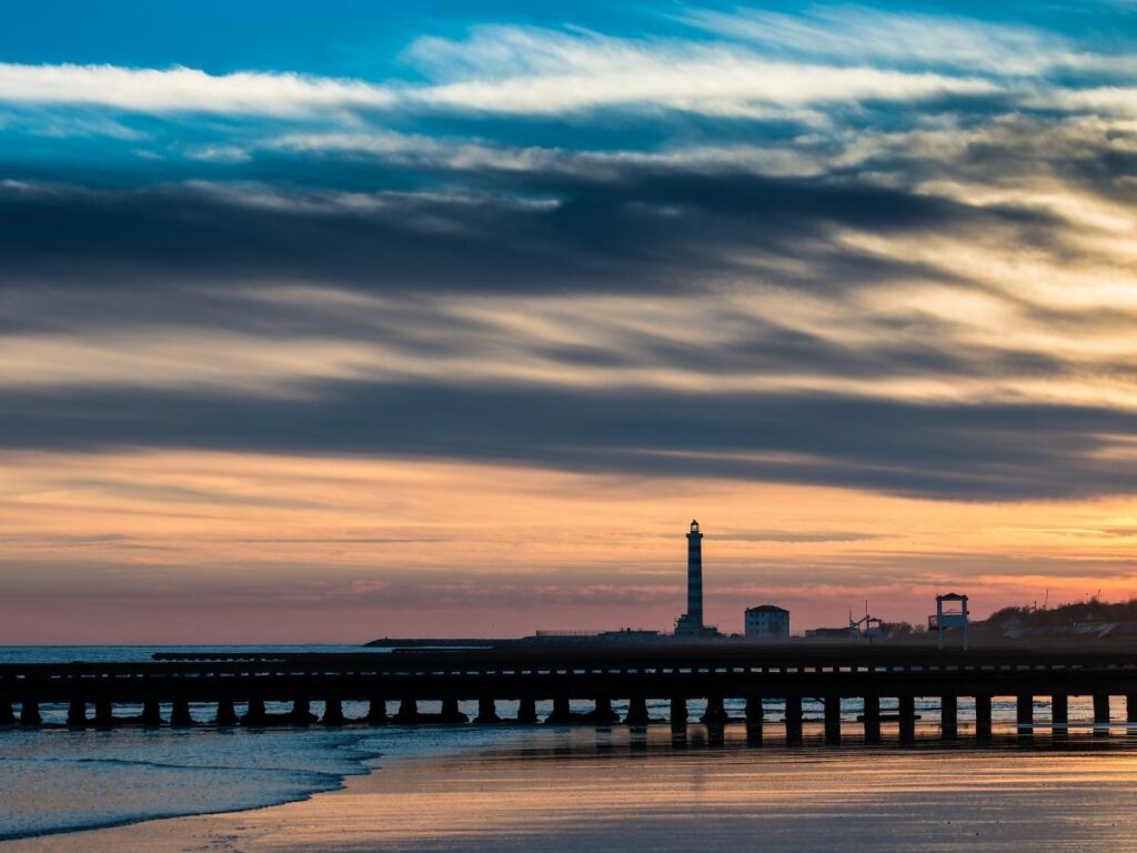 Jesolo’s lighthouse at Spiaggia del Faro silhouetted at sunset with people on the pier.