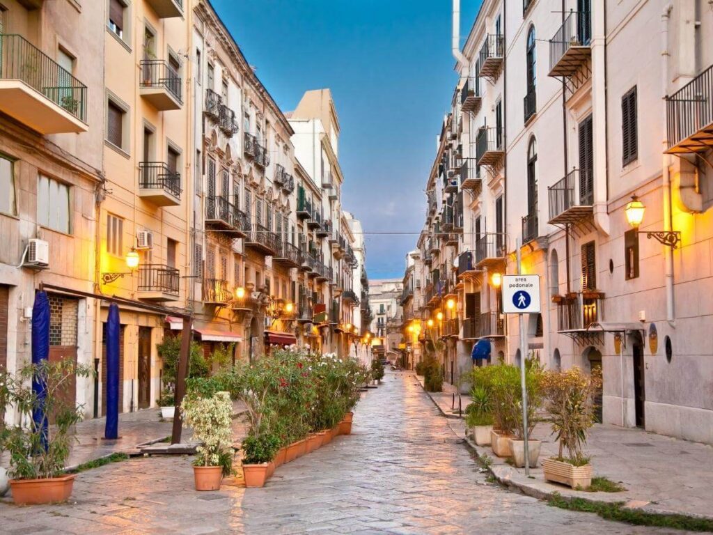 Colorful murals, hanging lights, and café tables along a side street in Palermo’s Kalsa district