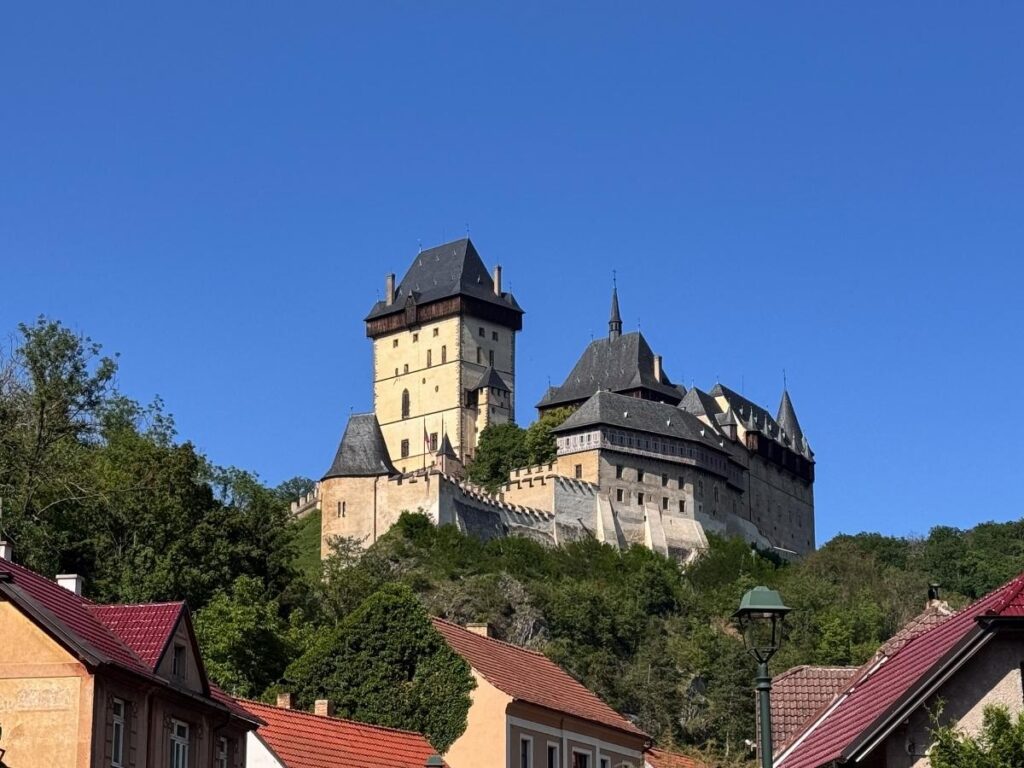 Karlštejn Castle perched on a forested hill with the countryside path and train tracks in the foreground