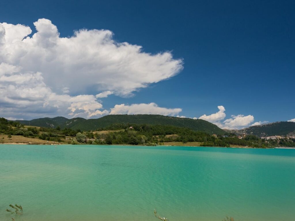 Turquoise waters of Lake Castel San Vincenzo surrounded by lush green hills.