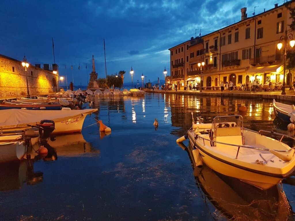 Sunset over Lazise waterfront with people walking the promenade and lights reflecting in the lake