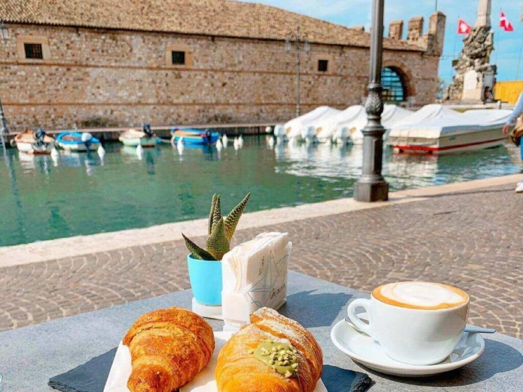 Coffee cup on a café table overlooking Lazise harbour in the early morning light