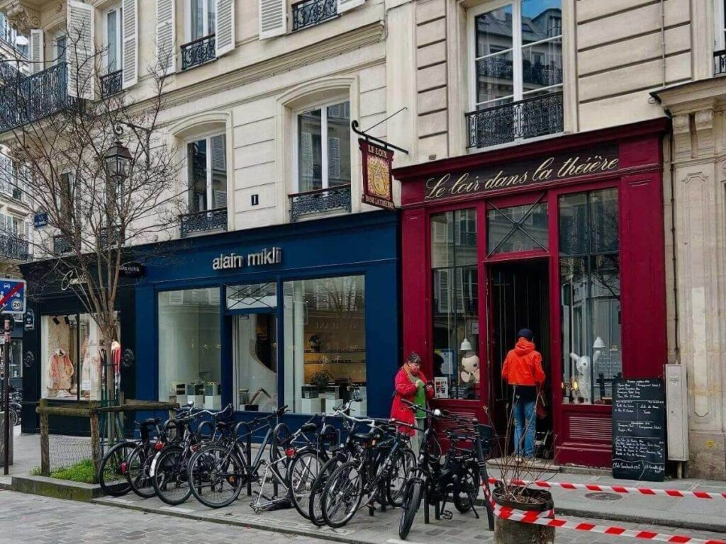 Boutiques and cafés along a cobblestoned street in Le Marais, Paris.