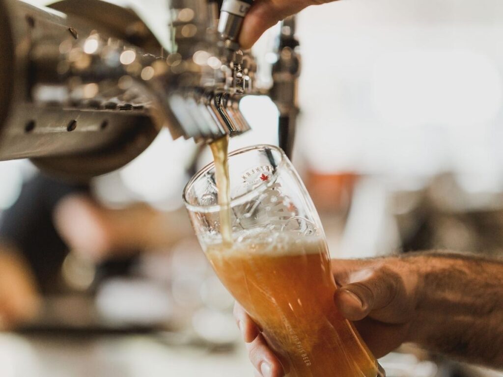 Close-up of a frothy Pilsner on a wooden table with Letná Park and Prague skyline blurred in the background