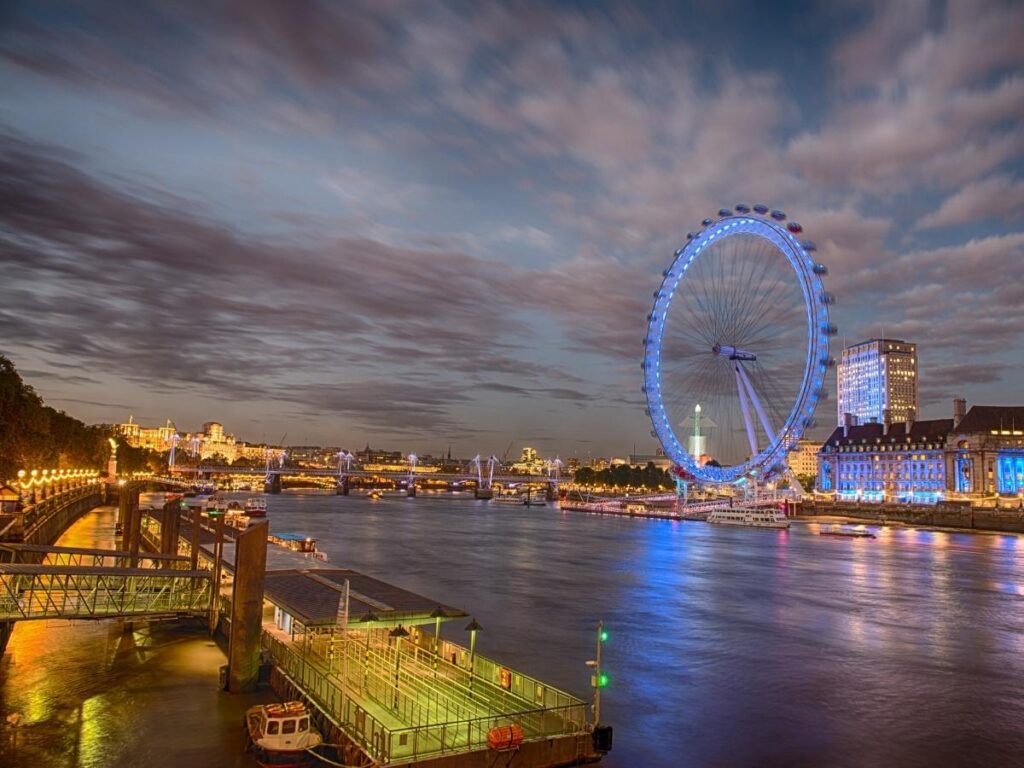 The London Eye illuminated at night, reflecting over the River Thames