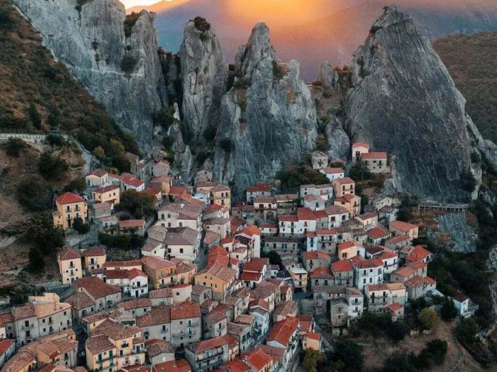 Panoramic view of the Lucanian Dolomites with rugged peaks and scattered villages under a blue sky.