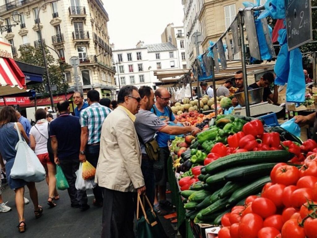 Vendors and shoppers at Marché d’Aligre market in Paris, with colorful produce stalls.