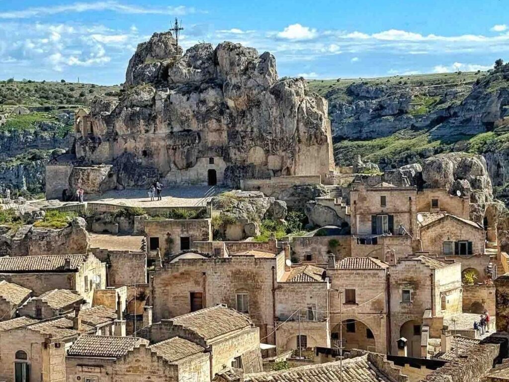 Interior of a restored cave hotel room in Matera showing arched stone walls and a small bedside lamp.