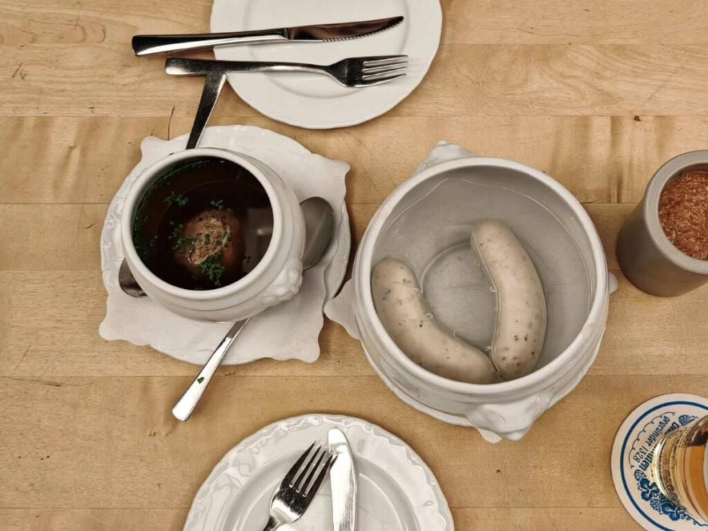 Traditional Bavarian breakfast with weisswurst sausages, pretzel, and sweet mustard served on a wooden table in Munich