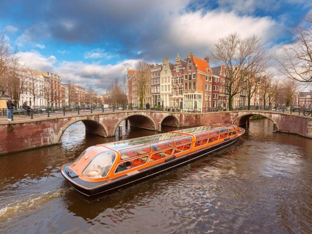 Small open canal boat cruising past historic canal houses in Amsterdam