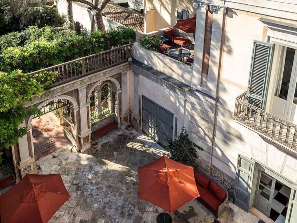 Elegant courtyard of Palazzo Margherita in Bernalda with stone arches, potted plants, and shaded seating.